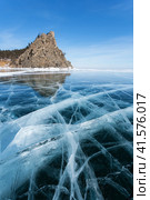 Scenic winter landscape of frozen Baikal Lake on sunny February day. View from blue ice with cracks to sandy beach of Peschanaya Bay and Kolokolnya Rock - natural landmark and place of attraction for tourists. Стоковое фото, фотограф Виктория Катьянова / Фотобанк Лори