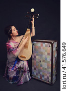 A happy female musician in Asian clothes on a studio black background. A smiling woman with a stringed musical instrument from Asia on a dark background. Стоковое фото, фотограф Андрей Журавлев / Фотобанк Лори