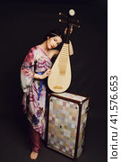 A happy female musician in Asian clothes on a studio black background. A smiling woman with a stringed musical instrument from Asia on a dark background. Стоковое фото, фотограф Андрей Журавлев / Фотобанк Лори