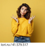 A young, pensive, insecure, rather attractive European girl of 20 years in a yellow casual blouse, spreads her hands questioningly, looking away. Created by AI. Стоковое AI-изображение, AI-художник Ярославский Максим / Фотобанк Лори