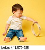 Toddler baby plays the tambourine, a child with a percussion musical instrument on a studio yellow background. Happy child musician playing hand drum. Kid aged one year four months. Стоковое фото, фотограф Андрей Журавлев / Фотобанк Лори