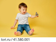 Toddler baby plays with a musical rattle bells on a stick, studio yellow background. Happy child musician playing percussion musical instrument, copy space. Kid aged one year and four months. Стоковое фото, фотограф Андрей Журавлев / Фотобанк Лори