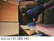 A man in gloves steals goods from a box in a warehouse. Problems with theft and security in the office. Стоковое фото, фотограф Андрей Журавлев / Фотобанк Лори