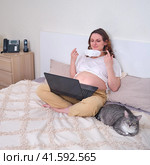 A pregnant woman puts on a face mask n95 ffp2. Study and work at home office during quarantine due to coronavirus. Стоковое фото, фотограф Андрей Журавлев / Фотобанк Лори