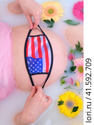 Pregnant woman belly in white bathroom with face mask n95 ffp2 and USA flag. Стоковое фото, фотограф Андрей Журавлев / Фотобанк Лори
