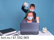 The child interferes with the mother behind the laptop at remote work in the face mask. Стоковое фото, фотограф Андрей Журавлев / Фотобанк Лори