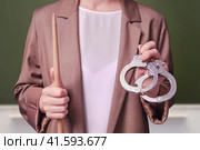 Woman teacher holding handcuffs in her hands on school blackboard in the classroom. Стоковое фото, фотограф Андрей Журавлев / Фотобанк Лори