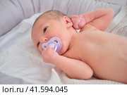 A newborn baby holds a pacifier in his mouth with his hand. Child boy in a cocoon on a crib. Стоковое фото, фотограф Андрей Журавлев / Фотобанк Лори