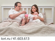 Mother and father with baby boy with money for upbringing, financial problems of parents with infant child. Man and woman consider family budget with newborn baby in bedroom. Стоковое фото, фотограф Андрей Журавлев / Фотобанк Лори