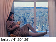 A pregnant woman sits by a winter window with a cup of coffee and holds her belly with her hand. Pregnancy and expectation of the birth of an unborn child. Стоковое фото, фотограф Андрей Журавлев / Фотобанк Лори