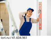 Woman in overalls checks the verticality of walls with a building level. Стоковое фото, фотограф Яков Филимонов / Фотобанк Лори