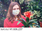 Adult woman gardener in medical mask chooses bromelia flowers in store. Buying indoor plants for home gardening with coronavirus quarantine. Стоковое фото, фотограф Андрей Журавлев / Фотобанк Лори
