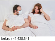 A woman thinks looking at a man lying in a medical mask in bed. Quarantine family problems due to coronavirus. Стоковое фото, фотограф Андрей Журавлев / Фотобанк Лори