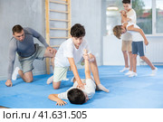 Focused boy learning effective self defence techniques in sparring with boy, practicing painful pronating wristlock on opponent lying face down on floor in gym. Стоковое фото, фотограф Яков Филимонов / Фотобанк Лори