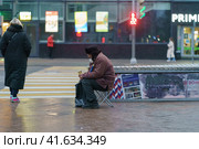 Moscow, Russia- November 13, 2020: Street life during coronavirus pandemic. People wear/ put on/ use protective face masks. Lifestyle concept. A beggar sits on a chair and begs for alms. Social image. Редакционное фото, фотограф YuryKara / Фотобанк Лори