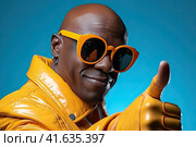 An African young man in a yellow jacket shows a thumbs-up against a blue sky. Generated by Ai . Стоковое AI-изображение, AI-художник Ярославский Максим / Фотобанк Лори