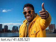 An African young man in a yellow jacket shows a thumbs-up against a blue sky. Generated by Ai. Стоковое AI-изображение, AI-художник Ярославский Максим / Фотобанк Лори