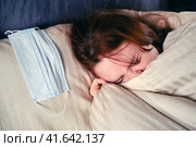 Redhead woman with a flu virus is covered with a blanket and squints while lying on the bed. Стоковое фото, фотограф Андрей Журавлев / Фотобанк Лори