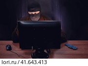 Hacker in balaclava steals information in the server room. Concept of data integrity issues and hacker attacks. Стоковое фото, фотограф Андрей Журавлев / Фотобанк Лори
