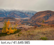 Colorful view to autumn mountain valley with forest and river against mountain range under cloudy sky. Wide mountain valley in mist and large mountains in lush clouds in changeable weather. Стоковое фото, фотограф Саблин Станислав / Фотобанк Лори