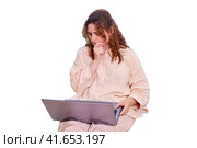 Sad woman student reflected while sitting on the bed with a computer, isolated on a white background. Doubting woman while studying online from home. Стоковое фото, фотограф Андрей Журавлев / Фотобанк Лори
