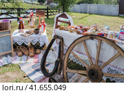 Клязьминский городок (Стародуб), Россия. Изделия народного промысла на ярмарке. Обрядовые куклы, колесо от телеги, конская упряжь, лапти, чугунок, скатерть, полотенце, прялка, корзина. (2023 год). Редакционное фото, фотограф Сергей Никифоров-Гордеев / Фотобанк Лори