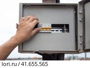 A man switches the toggle switches of the electrical panel on the pole. Electrical input, safe connection. (2023 год). Редакционное фото, фотограф Коханова Наталья / Фотобанк Лори