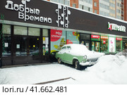 Odintsovo, Russia - January 2, 2022. Snow covered Soviet oldtimer GAZ-21 Volga in front of Dobrye Vremena (Good Times) shop in Nedelin street. Cloudy winter view. Магазин антиквариата "Добрые времена" в Одинцово. Редакционное фото, фотограф Александр Кузнецов / Фотобанк Лори