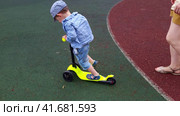 A baby learns to ride a children scooter. A mother woman teaches a child to ride a scooter. Kid boy aged two years (two-year-old) Стоковое видео, видеограф Андрей Журавлев / Фотобанк Лори