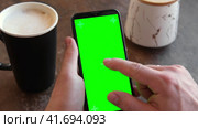 Man Use of Mobile Phone with Blank Green Screen in a Cafe on Rustic Vintage Wooden Table. Male Holding Smart Phone Empty ChromaKey Screen Mock up in Coffee Shop. Morning. Showing Mock up Video Footage. Стоковое видео, видеограф Марина Демидюк / Фотобанк Лори