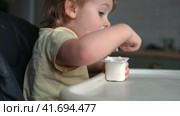 Toddler Sitting in Highchair Eating Greek Yogurt. Funny Cute Baby Eats in the Kitchen. Little Girl Learning to Eat. Child Feeding Himself by Silicone Spoon at Home. Breakfast with Dairy Products. 4K. Стоковое видео, видеограф Марина Демидюк / Фотобанк Лори