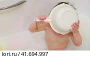 Baby drinks water from a ladle while sitting with toys in a white bathtub A happy child enjoys washing in the bathroom. Kid about two years old (one year ten months). Стоковое видео, видеограф Андрей Журавлев / Фотобанк Лори