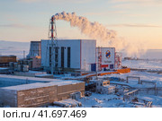 Крупная тепловая электростанция в Арктике. На стене логотип энергетической компании «РусГидро». Шлейф дыма из промышленной трубы. Холодная погода. Город Анадырь, Чукотка, Россия. Редакционное фото, фотограф Андрей Степанов / Фотобанк Лори