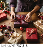 An unrecognizable woman wraps Christmas gifts in craft paper. Стоковое AI-изображение, AI-художник Margarita Davchenko / Фотобанк Лори