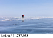 BAIKAL LAKE, GOLOUSTNOYE VILLAGE, IRKUTSK REGION, RUSSIA - March 13, 2021: Couple of tourists skating on blue ice of frozen Baikal lake on sunny warm day in March. Outdoor activities. Редакционное фото, фотограф Виктория Катьянова / Фотобанк Лори