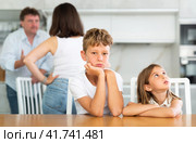 Two children sitting at the kitchen table sadly while their parents quarrelling. Стоковое фото, фотограф Яков Филимонов / Фотобанк Лори