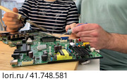 Close-up of a man teaching his boy at home to solder computer spare parts. Young father with his son spend time together. Education moment during parenthood. Togetherness concept. Стоковое видео, видеограф Ирина Старикова / Фотобанк Лори