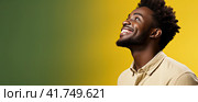 A young African man in a T-shirt on a uniform background looks up and smiles. Generated by AI. Стоковое AI-изображение, AI-художник Ярославский Максим / Фотобанк Лори