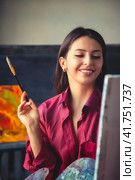 Portrait of perfect young woman painter in red shirt sitting at home studio workshop, smiling look. Happy lovely lady artist paints at canvas with paint oil. Painting at art studio. Copy ad text space. Стоковое фото, фотограф Aleksandr Golubev / Фотобанк Лори