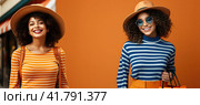 Two beautiful brunette with curly hair in sunglasses posing in front of the camera in a yellow studio. Стоковое AI-изображение, AI-художник Ярославский Максим / Фотобанк Лори