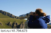 A woman with glasses is sightseeing through tourist binoculars in the mountains. Girl in windbreaker looking at mountains in sightseeing binoculars. Stepantsminda, Georgia August 22, 2022. Редакционное видео, видеограф Воловодов Владимир / Фотобанк Лори