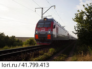 Локомотив ЭП1М с пассажирским составом едет по сельской местности. EP1M locomotive carrying a passenger train through a rural landscape. Summer sunset view. (2021 год). Редакционное фото, фотограф Александр Кузнецов / Фотобанк Лори