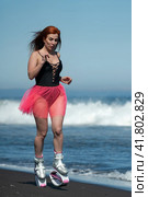 Woman athlete in Kangoo Jumps boots, one-piece swimsuit and short skirt running and jumping on black sandy beach during aerobic and fitness training (2022 год). Редакционное фото, фотограф А. А. Пирагис / Фотобанк Лори