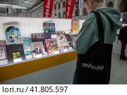 Посетитель ярмарки смотрит книги у стенда на международной ярмарке интеллектуальной литературы Non/fiction в Гостином дворе города Москвы, Россия (2023 год). Редакционное фото, фотограф Николай Винокуров / Фотобанк Лори