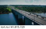 A modern asphalt highway winding away into the distance, winding through green meadows and forests, spanning over a bridge leading over a river. Drone shot. Стоковое видео, видеограф Даниил Хабаров / Фотобанк Лори