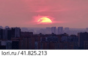 Big red sun over the roofs of city buildings, evening sunset. Timelapse of a cloudy sky and the sun setting behind the houses. Стоковое видео, видеограф Андрей Журавлев / Фотобанк Лори