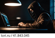 A man in mask with hood behind laptop. Symbol of group of hackers and anti system uprising against governments. Obscured dark face using computer for cyber attack, Data thief, internet attack. AI. Стоковое AI-изображение, AI-художник Sergey Grishin / Фотобанк Лори