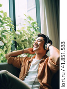 Asian mid adult men sitting near window with green house plants listening to music with headphones. Стоковое AI-изображение, AI-художник Наталья Семкина / Фотобанк Лори