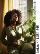 Adorable young dark skinned woman sitting with closed eyes near window enjoying sun beams. Стоковое AI-изображение, AI-художник Наталья Семкина / Фотобанк Лори