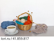 Still life with a cup of green tea and a basket with knitting and needlework. Balls and skeins of wool yarn and knitting needles on the table. Autumn knitting, DIY concept, close-up, copy space. Стоковое фото, фотограф Виктория Катьянова / Фотобанк Лори